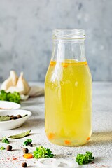 Homemade chicken (bone) broth (bouillon) with vegetables, spices and herbs in a glass bottle on a light background. Natural collagen of animal origin. Liquid broth from meat, fish, vegetables.