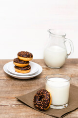 Mini donuts covered with chocolate glaze served with bottle, jug, glass of milk. Stack of tasty sweet sugar creamy or icing doughnuts dessert food on plate and napkin on kitchen. national donuts day