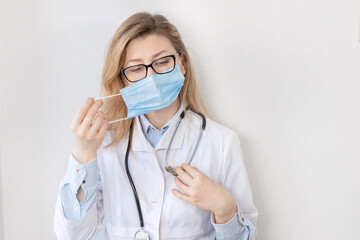 Portrait of female doctor putting on a blue protective mask, cover up her face. Caucasian woman in medical uniform is looking at the camera, reminds to take care of yourself while coronavirus pandemic