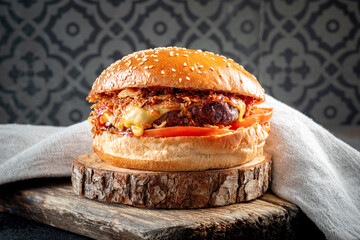 A plump burger with beef, fried onions, cheese, tomatoes and barbecue sauce on a wooden board....