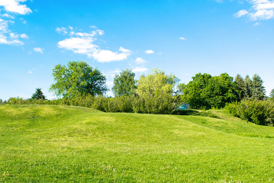 Scenic view of beautiful small mountains, hills, mounds with green grass lawn against bright blue sky with clouds in city park