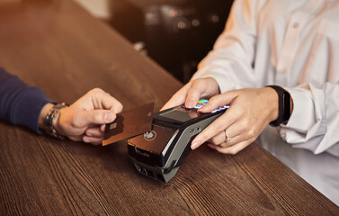 The customer's hand pays for a contactless credit card with NFC technology. Bartender with a Credit Card reader. Focus on hands.