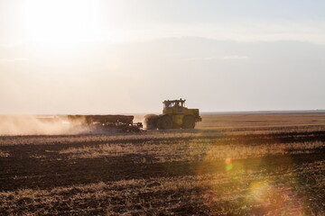 Kostanay Province, Kazakhstan - May 01, 2019: Tractor seeds wheat in field on sunset. Sowing season.