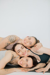 three beautiful women smiling bowed their heads over each other, hugging each other.
girls rest after yoga practice and meditate in a women's circle on a white background
