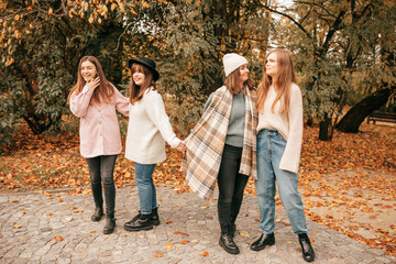 Four close female friends company reunion after university, spending time together, holding hands in autumn gold park