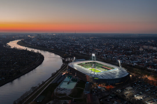 Beautiful aerial sunset cityscape and skyline of Bermen. Illuminated Weserstadion, home stadium of football club SV Werder Bremen. Bremen, Germany - March 2022
