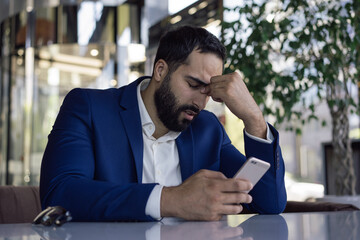Stressed tired Moroccan businessman using mobile phone missed deadline, having headache sitting in...