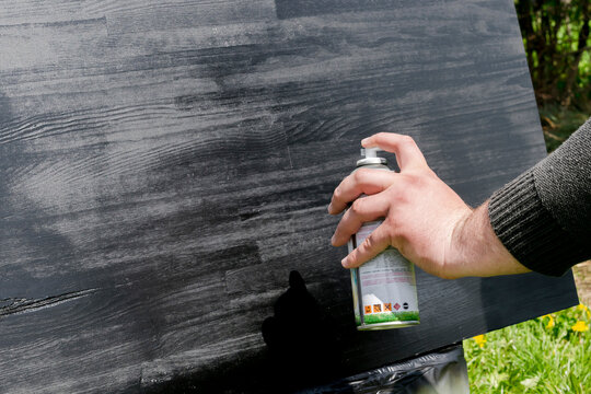 Mans male hand painting wood with black spray paint. Worker applying varnish paint on wooden table board surface, painting and caring for wood. House home renovation, copy space, texture