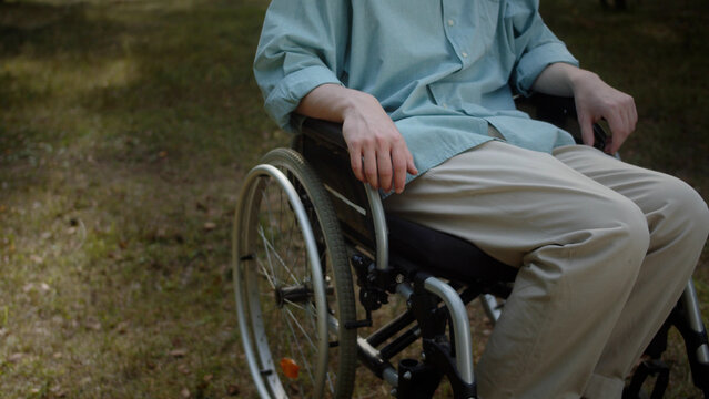 A young white disabled man in the wheelchair is sitting in the park and looking at the camera smiling, close-up
