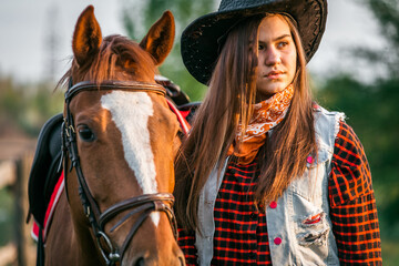 Obraz premium A cowgirl stands near her horse in a field at sunset.