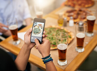 Look at this amazing pizza. Shot of a unrecognizable person taking a photo of a few pizzas on a table outside at a restaurant.
