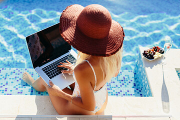 freelancer woman using laptop and work remotely near swimming pool. Sexy woman freelancer browsing...
