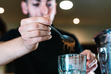 detail of the hands of a young waiter, adding brown sugar in a large crystal glass to prepare a Mojito. horizontal.