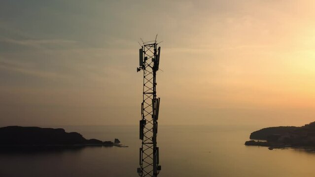Amazing closeup sunset drone view of silhouette of cell tower. Wireless connection. Spectacular view of cellular tower with mountains and sea in the background. 5G network. Сell site