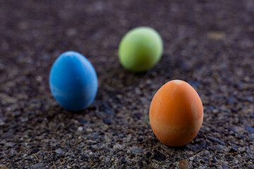 Chalk eggs of orange, blue and green sitting on stunning cement near Easter holiday.