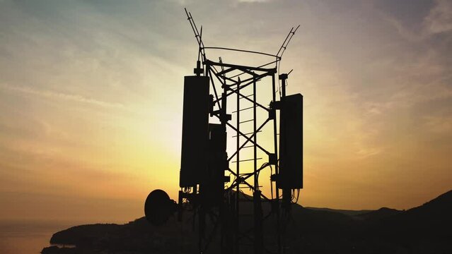 Amazing closeup sunset drone view of silhouette of cell tower. Wireless connection. Spectacular view of cellular tower with mountains and sea in the background. 5G network. Сell site