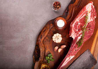cut of raw meat short rib marbled with fat and bone on stone with spices and cleaver on wooden board top view in the corner