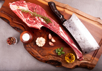 cut of raw short rib meat marbled with fat and bone on stone with spices and cleaver on wooden board top view in the center