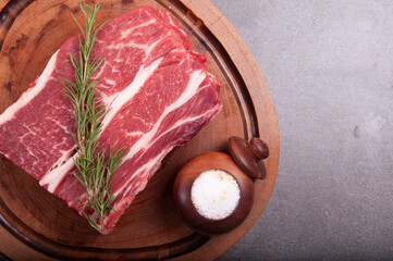 raw meat cut with fat denver steak in butcher shop on wooden board with rosemary and coarse salt close-up