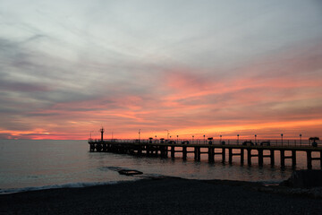 Obraz premium Fishing pier on the ocean with a colorful and golden sunset. Ocean beach sunrise and dramatic colorful sky clouds.