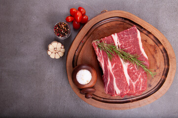 raw meat cut with fat denver steak in the butcher's shop on wooden board with rosemary and coarse salt, garlic, black pepper top view