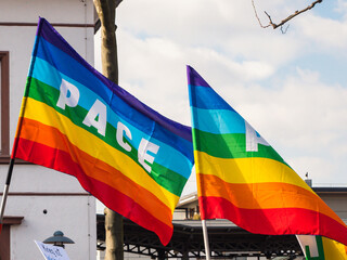 Rainbow flags when in the wind at a peace demonstration. The word pace is painted on the flags. 
