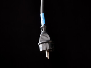 A plug with a power cord hangs in front of a black background. The plug is not plugged in. Copy...