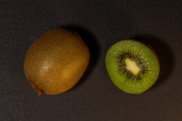 Kiwi fruits on black background. Whole kiwi and cut in half. Top view with copy space, flat lay.