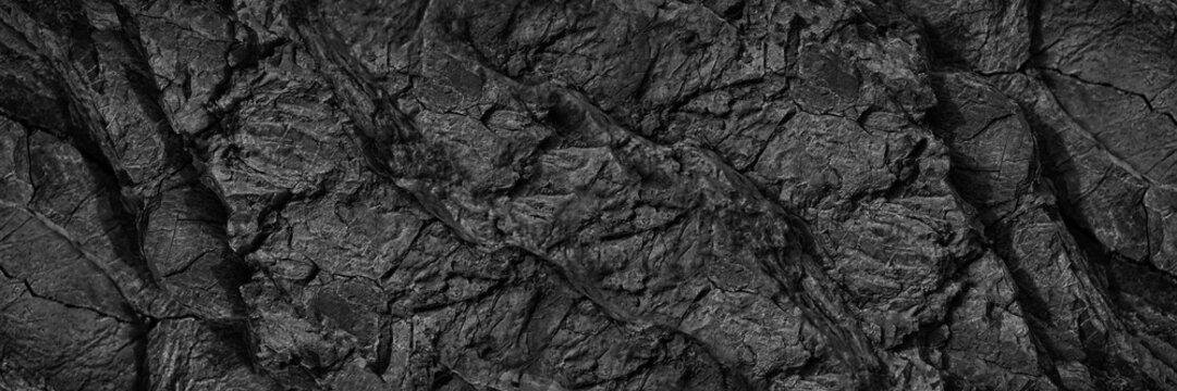 Black white rock texture. Dark gray stone wall background with space for design. Cracked rough mountain surface. Close-up. Wide banner. Panoramic. Granite backdrop. Grunge.