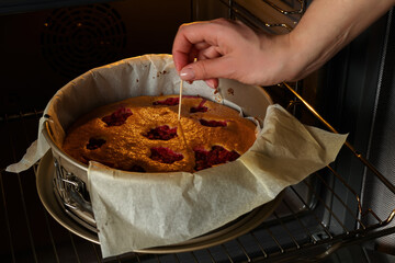 The girl tries with a toothpick the readiness of freshly baked raspberry pie in the oven. Pie with berries. Cozy food