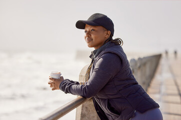 Good coffee and good views. Shot of a young woman enjoying a cup of coffee by the ocean.