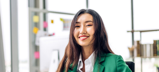 Beautiful confident asian businesswoman looking at desktop computer while sitting on office desk.Young creative coworkers business people working and planning