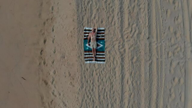 Man on beach in Mexico. Establishing beverage brand shot 4K drone. Slow pull up.