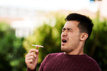Fototapeta premium Hayfever season. Cropped shot of a young man sneezing after smelling a flower.