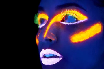 Neon celebration. A young woman with with neon paint on her face posing. © Tylan E/peopleimages.com