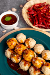 Fried pork meatballs skewers bamboo on a green plate with spicy sauce on a table,
fried pork tendon meatballs Thai street food.