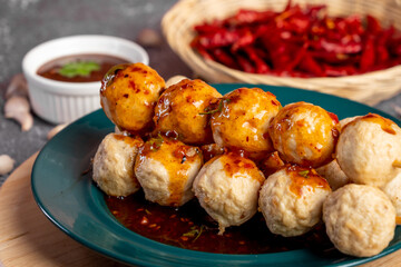Fried pork meatballs skewers bamboo on a green plate with spicy sauce on a table,
fried pork tendon meatballs Thai street food.