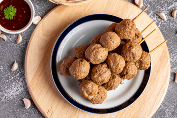 Fried beef meatballs skewers bamboo on a white plate with spicy sauce on a table,
fried beef tendon meatballs Thai street food. 