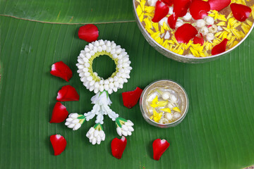 Beautiful Traditional Jasmine garland with colorful flower petals toping on water in bowl , Songkran festival background on green banana leave