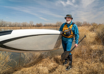 happy senior male paddler with his paddleboard and paddle on a lake shore in Colorado in early...