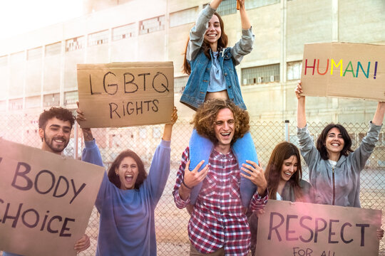 Group of excited and smiling diverse people marching for LGBT rights holding banners. Protesters march for LGBTQ rights.