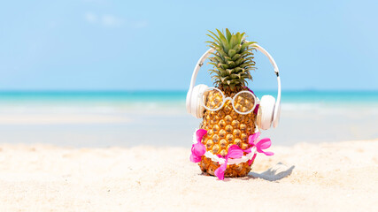 Summer in the party.  Hipster Pineapple Fashion in sunglass and listen music with sunblock and sandal on the sand beach beautiful blue sky background.  Creative art fruit for tropical style