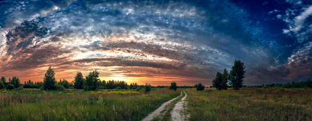 Sunset sky over green field at springtime or summertime, rural landscape panorama.