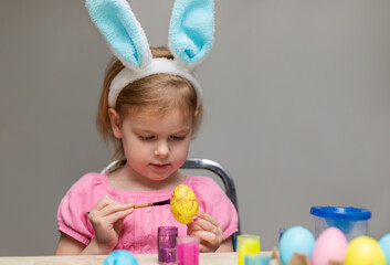 Little girl in Easter bunny ears painting Easter egg. Holiday crafts for kids.