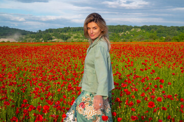 Happy woman resting on a beautiful poppy field. Girl having fun spring outdoor. Woman in field with red poppies.