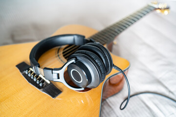Acoustic guitar and over-ear headphones on bed