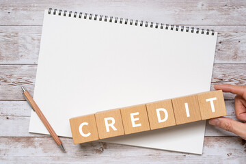 「CREDIT」と書かれた積み木、ノート、ペン、手
