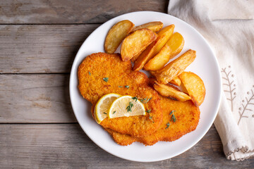 Chicken schnitzel with sauce, fried potatoes and lemon in a plate