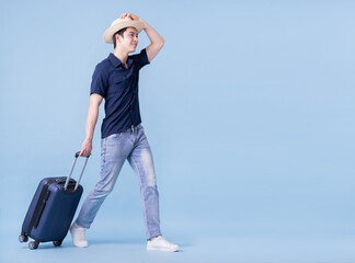 Image of young Asian man holding suitcase on blue background, travel concept