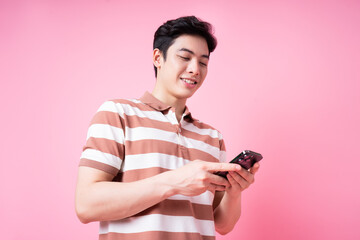 Portrait of young Asian man using smartphone on pink background